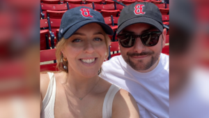 man and woman sitting in stadium with baseball hats