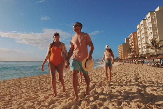 Family walking along beach with ocean on the left and a hotel on the right